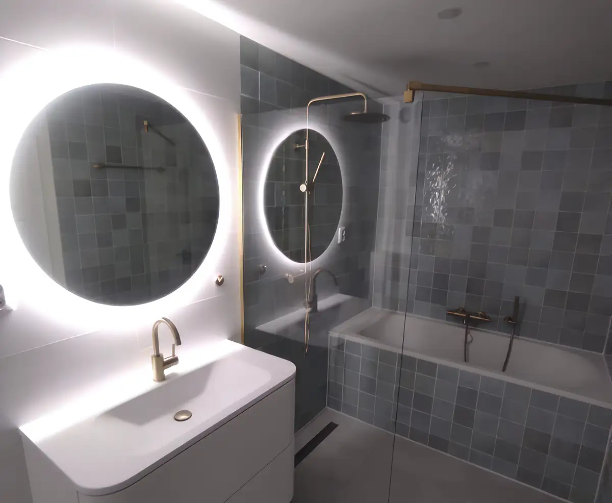A bathroom with green tiles and round lit mirrors