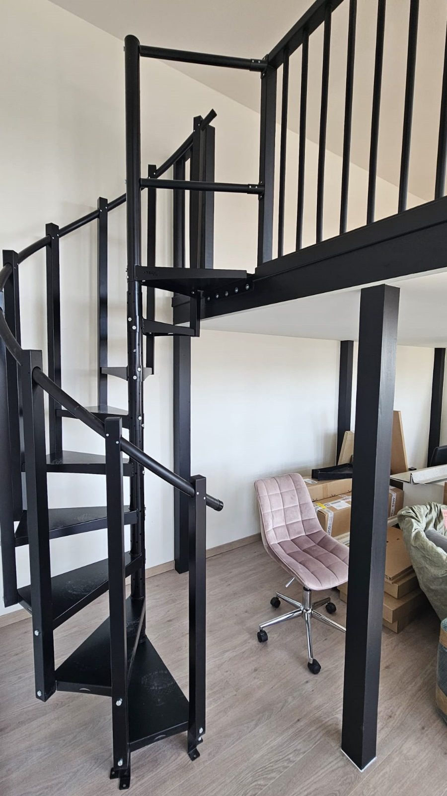 A black spiral stair leading up to a mezzanine