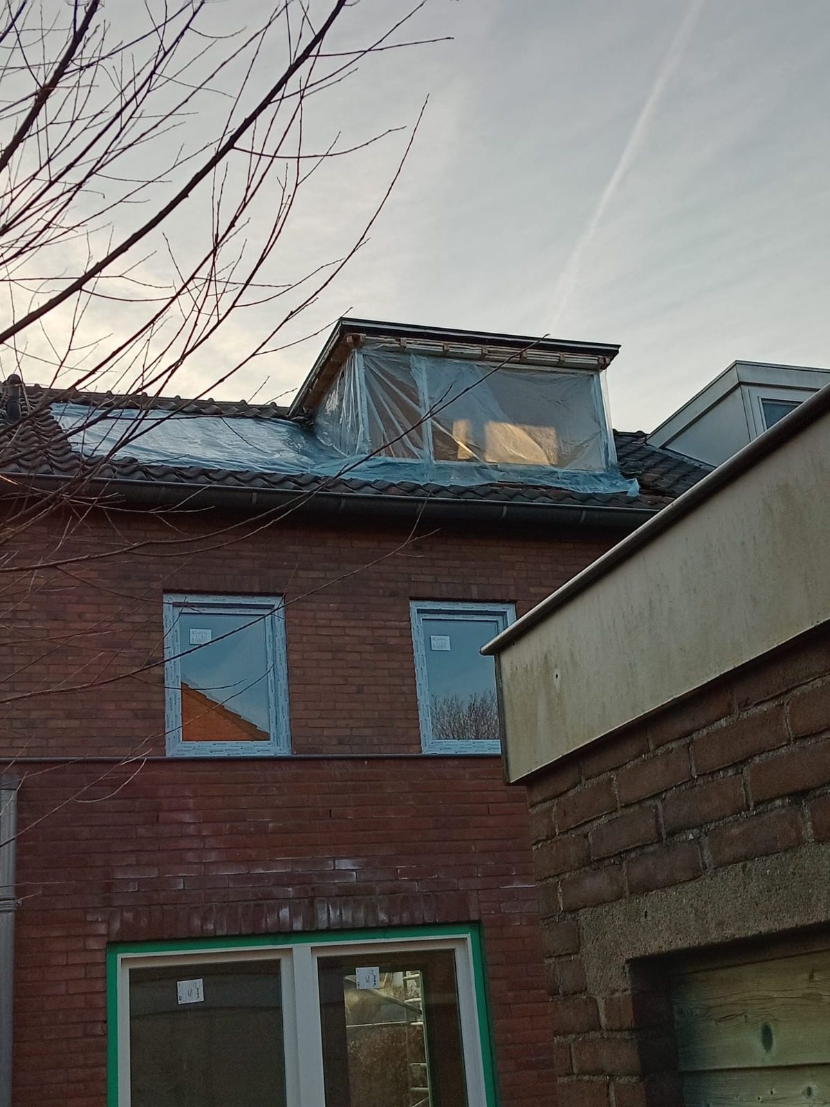 A new dormer on the back of a brick house, its windows still under protective foil