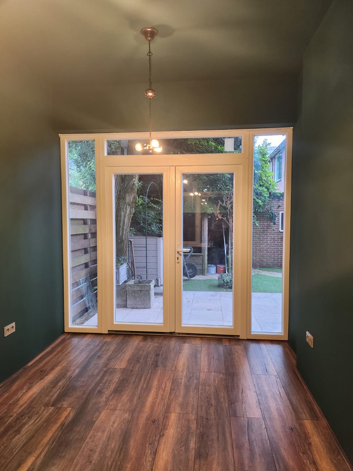 A finished extension with dark green walls, a wood floor and glass double doors to the garden