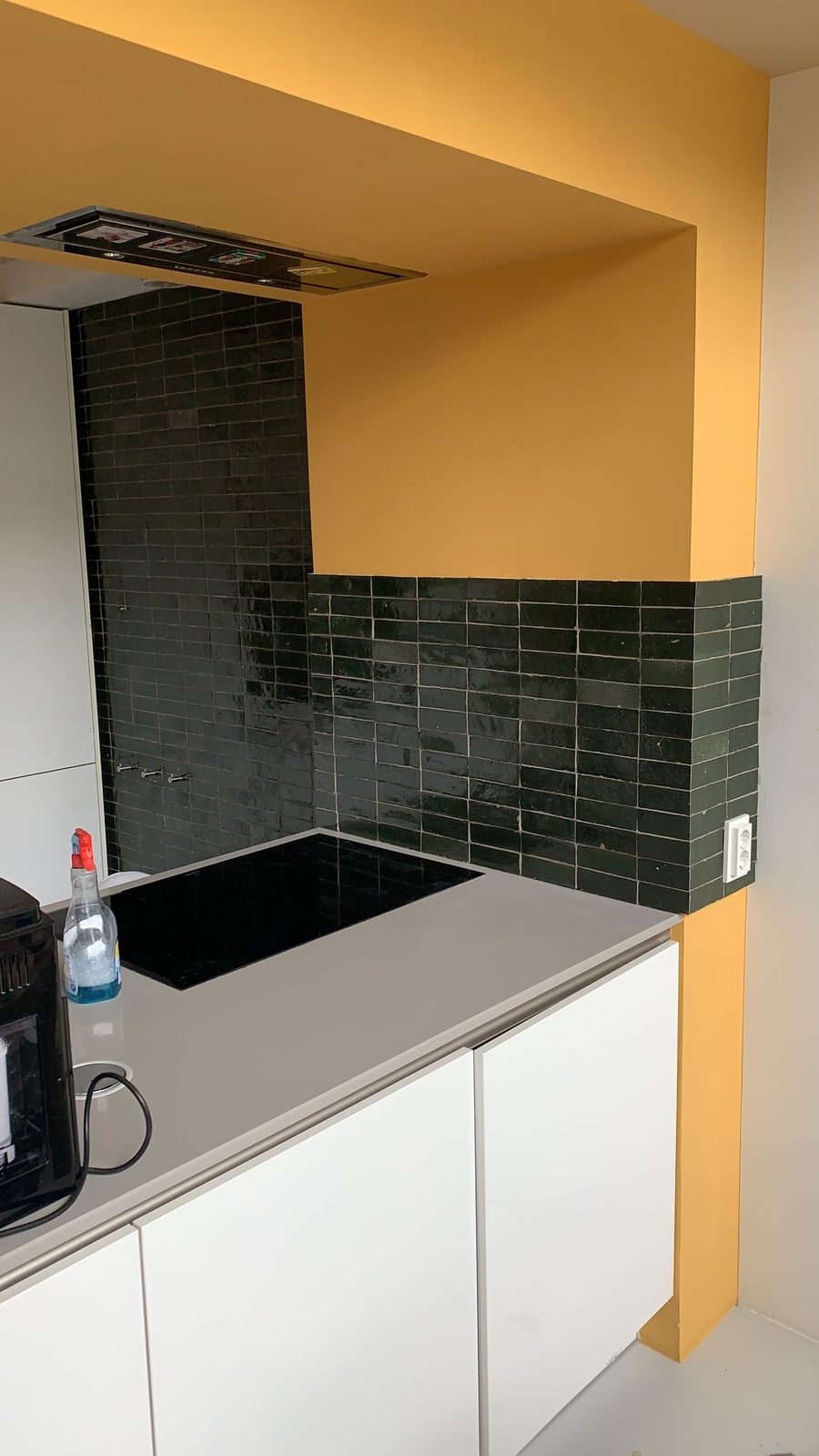 A wall of dark green glazed tiles behind the hob