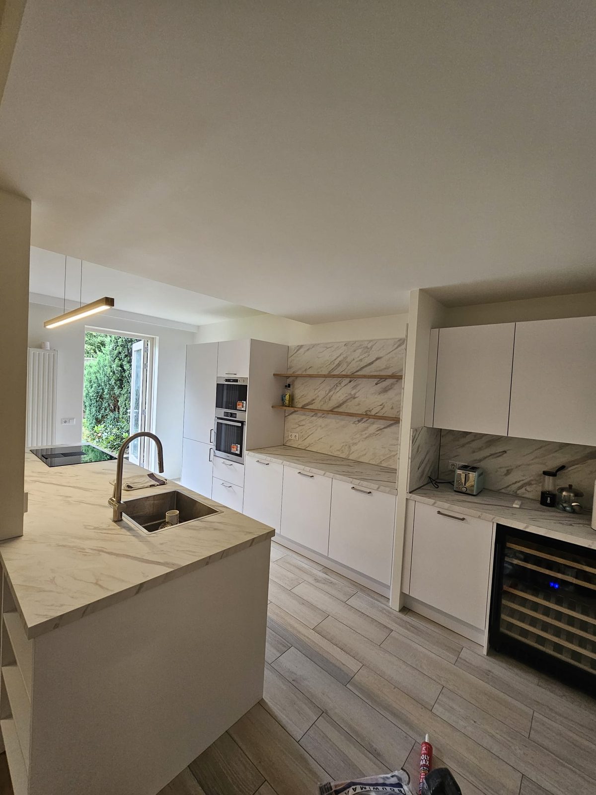 An open kitchen with a white island, a marble-look worktop and open shelves on the wall
