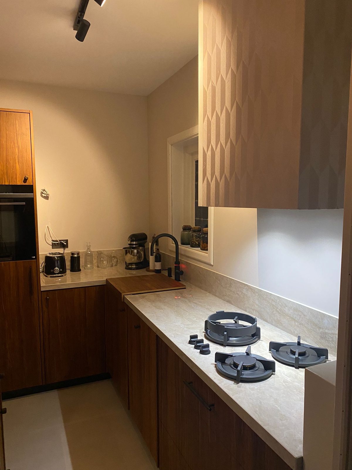 Walnut kitchen units with a gas hob and a light stone-look worktop