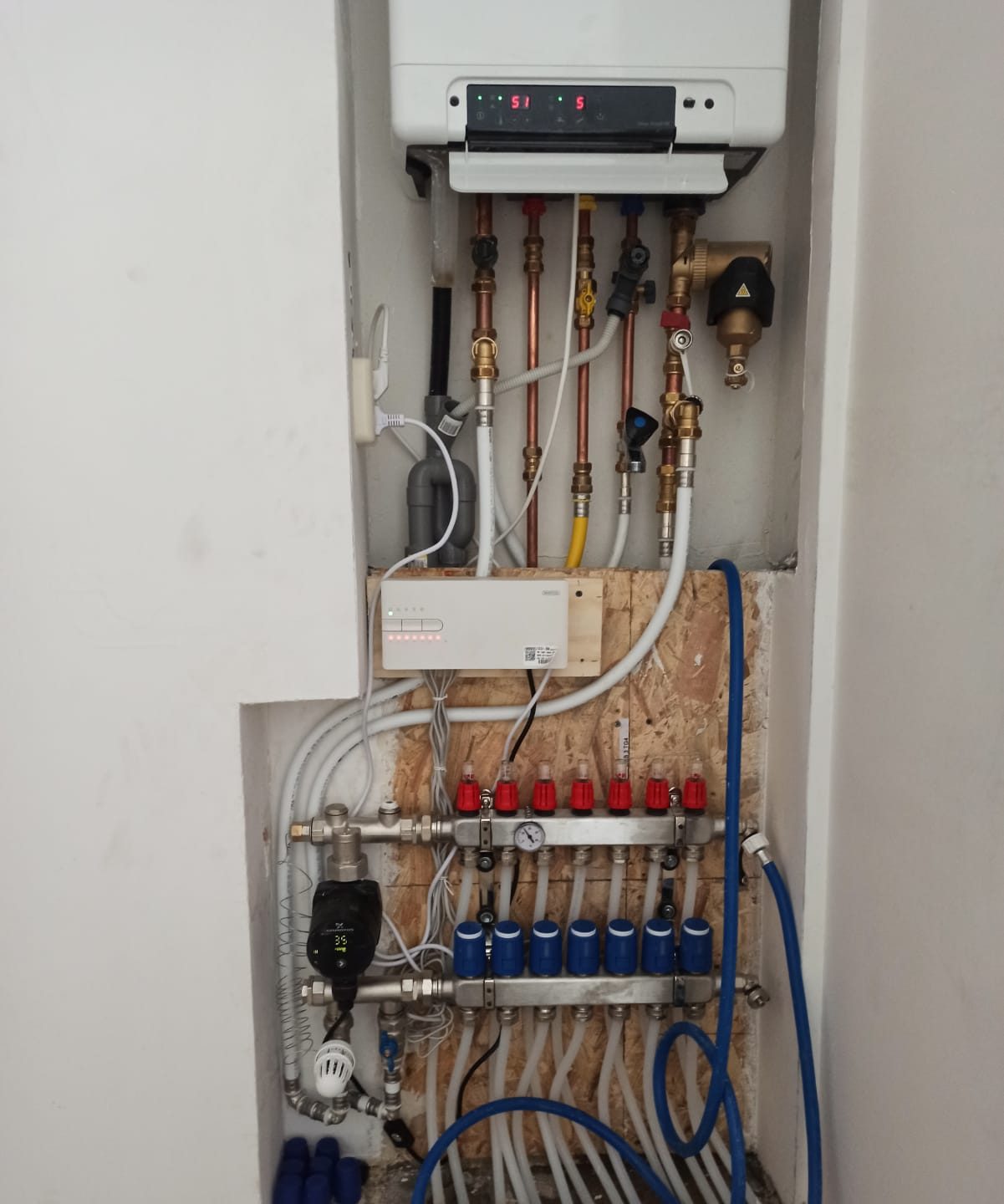A manifold with red and blue valves below a central heating boiler